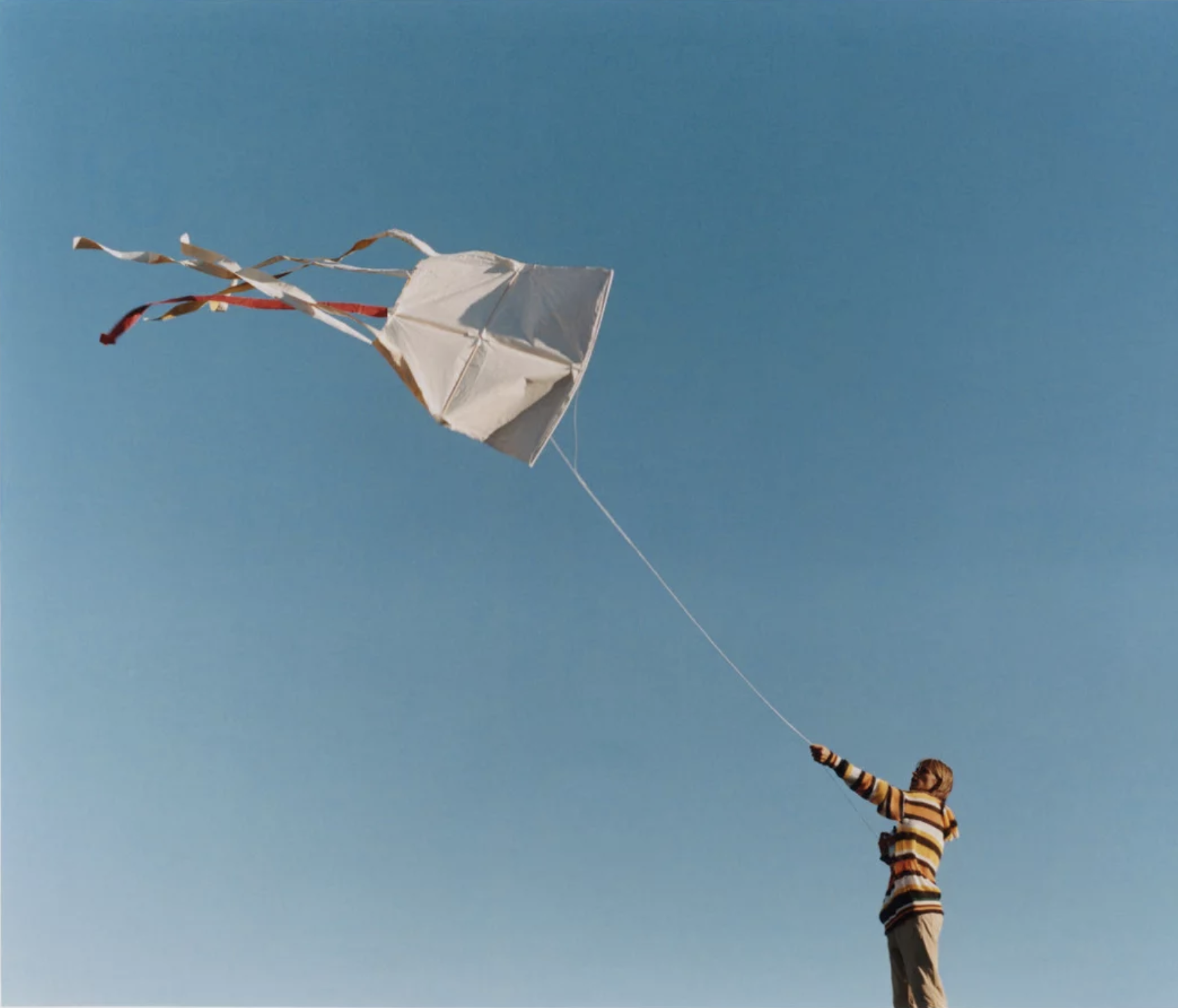 A child flying a white kite against a clear blue sky